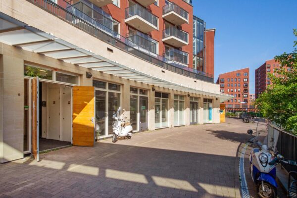 Ingang van een modern appartementencomplex aan het Harriet Freezerhof met scooters geparkeerd op een zonnige binnenplaats.